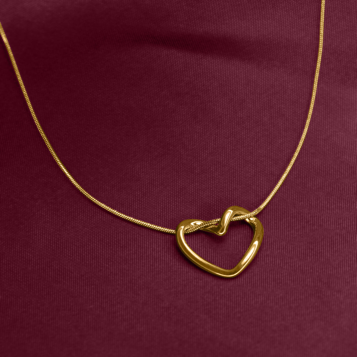 Gold heart-shaped necklace on a burgundy fabric background
