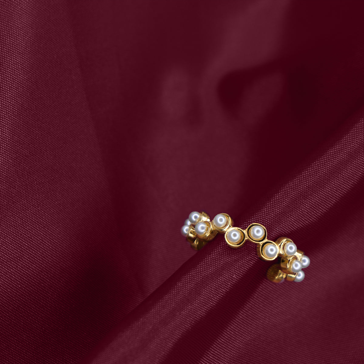 Gold earring with pearls on a burgundy fabric background